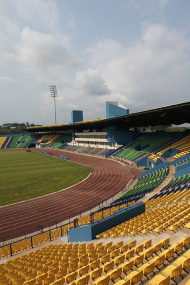 Stade en plein air avec gradins jaunes et vue sur la piste d'athlétisme et le terrain.